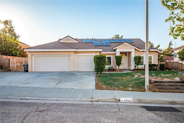 ranch-style house featuring a garage, fence, driveway, a tile roof, and solar panels