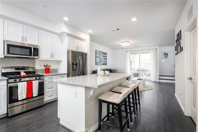 kitchen with stainless steel appliances, a kitchen island, white cabinetry, a breakfast bar, and light stone counters
