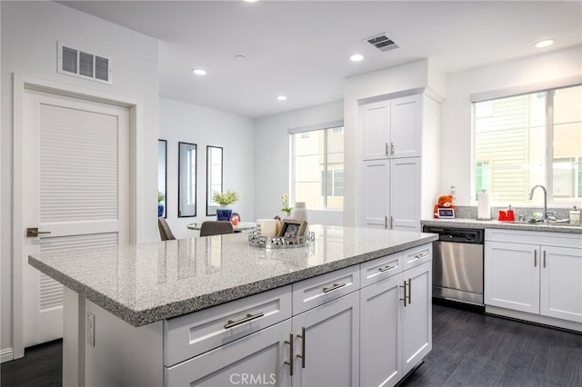 kitchen with stainless steel dishwasher, a sink, dark wood finished floors, white cabinets, and light stone counters