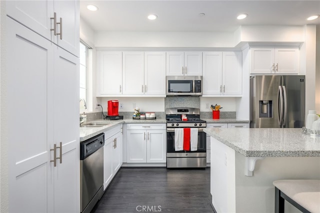 kitchen featuring appliances with stainless steel finishes, a sink, white cabinets, light stone countertops, and dark wood-style floors