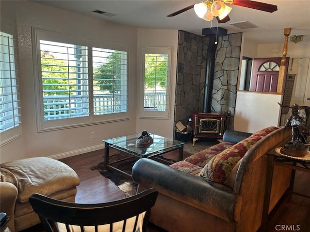 living area featuring ceiling fan, a wood stove, baseboards, wood finished floors, and visible vents