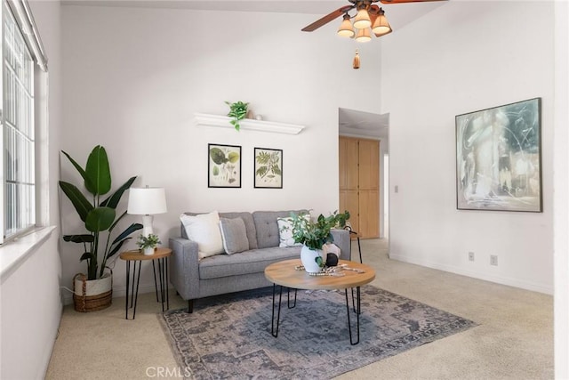 living room with baseboards, a ceiling fan, carpet flooring, and a towering ceiling