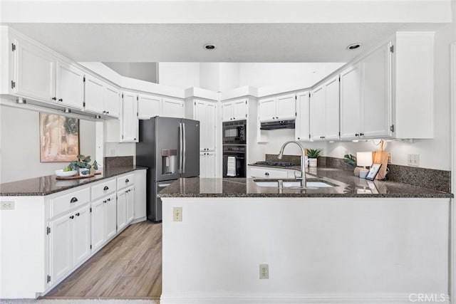 kitchen featuring a peninsula, dark stone counters, under cabinet range hood, a sink, and black appliances