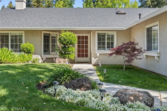 doorway to property featuring a lawn, stucco siding, a chimney, and a shingled roof
