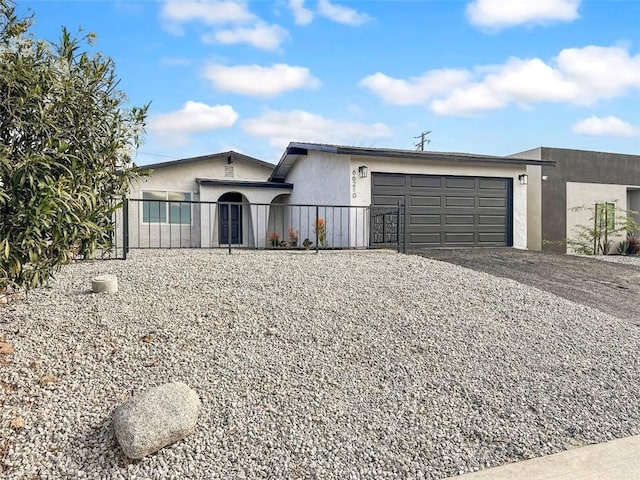 ranch-style house featuring a garage, stucco siding, gravel driveway, and fence