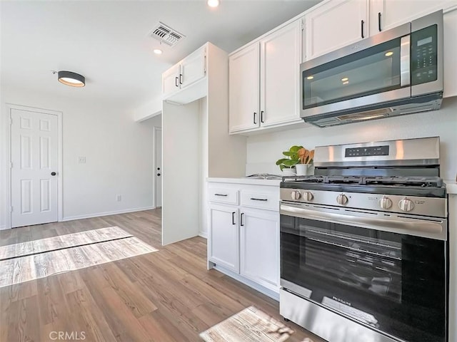 kitchen featuring white cabinets, stainless steel appliances, visible vents, and light wood-style floors