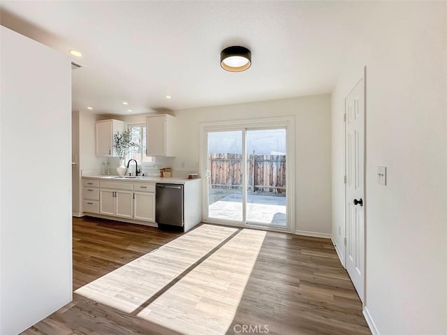 kitchen with dark wood-style flooring, dishwasher, light countertops, baseboards, and white cabinetry