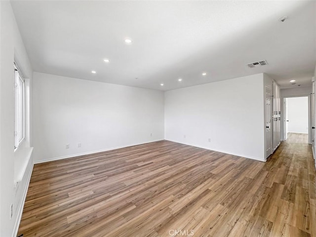 empty room with baseboards, recessed lighting, wood finished floors, and visible vents