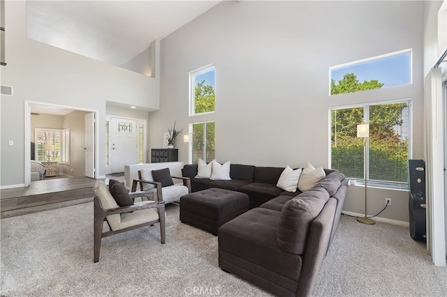living area featuring baseboards, visible vents, carpet, and a towering ceiling