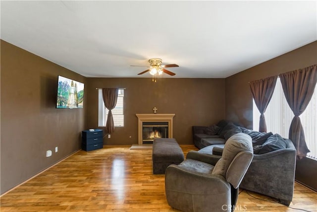 living area with ceiling fan, a glass covered fireplace, baseboards, and light wood-style floors