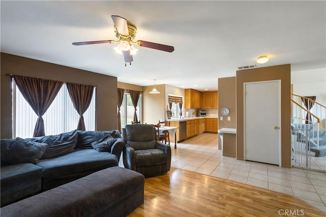 living area with light tile patterned floors, ceiling fan, stairs, and visible vents