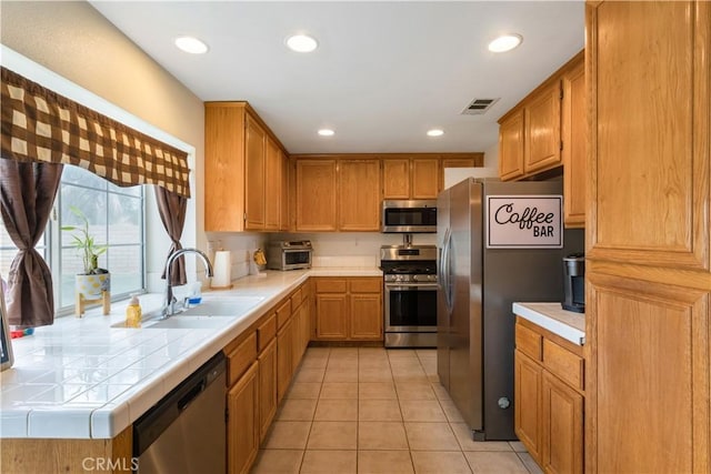 kitchen featuring light tile patterned flooring, appliances with stainless steel finishes, a sink, tile countertops, and visible vents