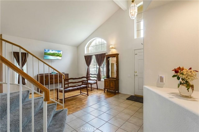 foyer with a healthy amount of sunlight, high vaulted ceiling, stairway, and light tile patterned flooring