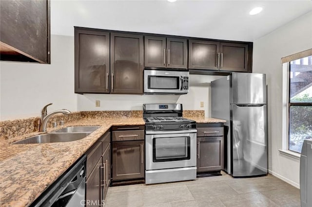 kitchen featuring dark brown cabinetry, appliances with stainless steel finishes, light stone countertops, a sink, and recessed lighting