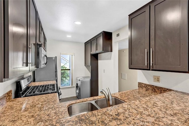 kitchen with dark brown cabinetry, appliances with stainless steel finishes, a sink, visible vents, and washing machine and dryer