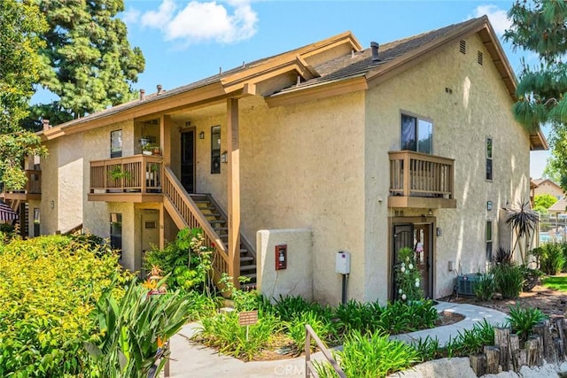 view of front of property with stairway, central AC, a balcony, and stucco siding