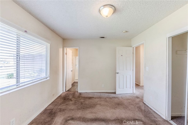 unfurnished bedroom featuring carpet floors, a textured ceiling, visible vents, and baseboards