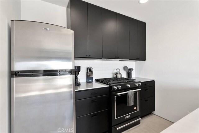 kitchen with black gas stove, light countertops, dark cabinets, freestanding refrigerator, and tasteful backsplash