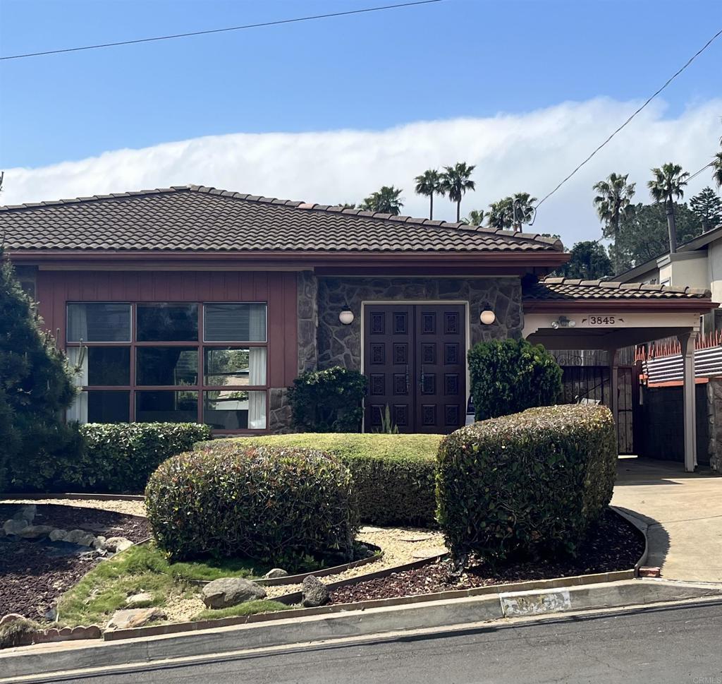 view of front facade featuring driveway, a tile roof, stone siding, and an attached carport