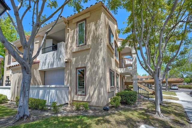 view of side of property with stucco siding, a balcony, and stairway