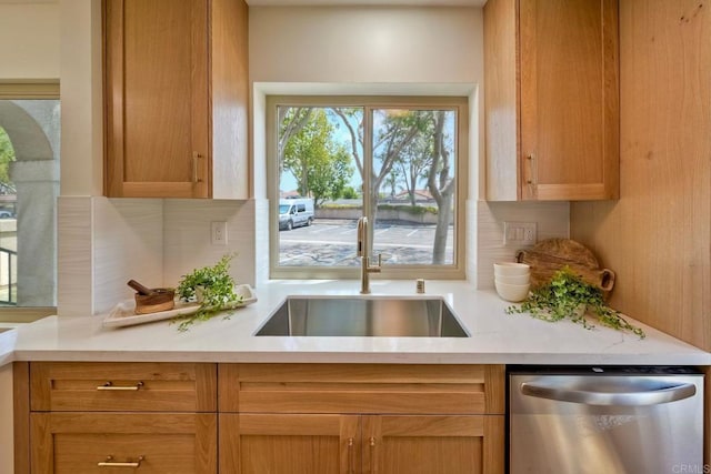 kitchen featuring stainless steel dishwasher, a sink, decorative backsplash, and light countertops