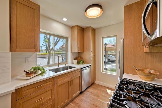 kitchen with light wood-style floors, light countertops, a sink, backsplash, and stainless steel appliances