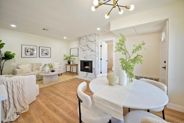 dining space with visible vents, a fireplace, recessed lighting, light wood finished floors, and a notable chandelier