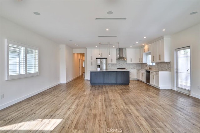 kitchen with wall chimney range hood, stainless steel appliances, open floor plan, and white cabinets