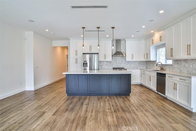 kitchen with wall chimney range hood, white cabinets, a sink, stainless steel appliances, and a kitchen island