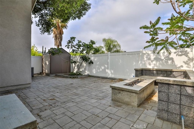 view of patio / terrace with a fenced backyard, an outdoor structure, an outdoor fire pit, and a shed