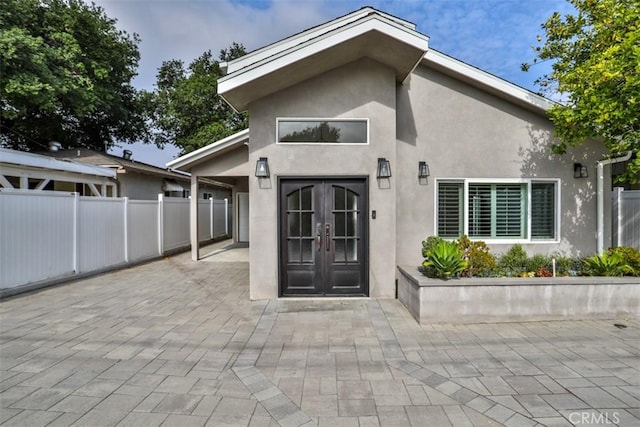 property entrance with a patio, stucco siding, fence, and french doors