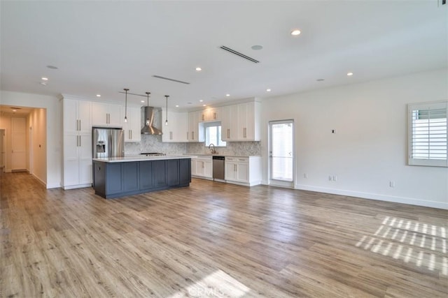 kitchen featuring white cabinetry, light countertops, open floor plan, stainless steel appliances, and wall chimney exhaust hood