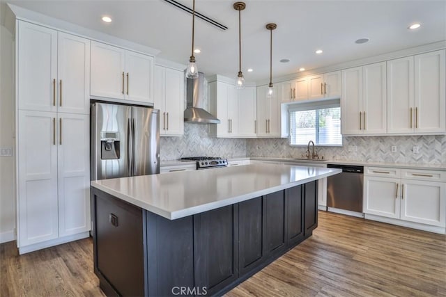 kitchen with a kitchen island, wall chimney range hood, white cabinets, a sink, and stainless steel appliances
