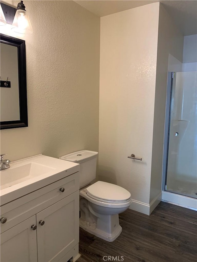 bathroom with a shower stall, wood finished floors, vanity, baseboards, and toilet