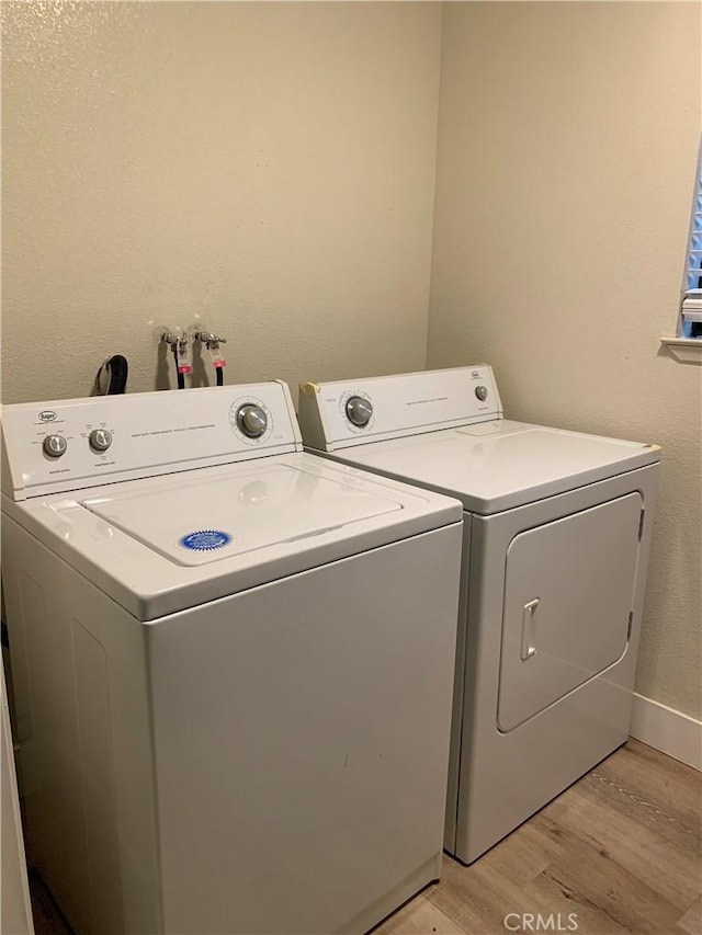 washroom featuring separate washer and dryer, laundry area, baseboards, and light wood-type flooring