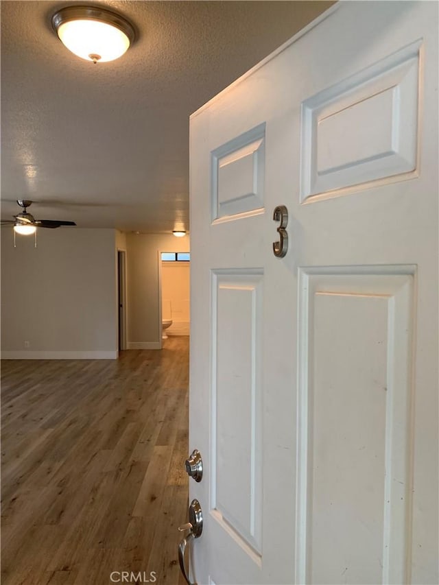 corridor with baseboards, a textured ceiling, and wood finished floors