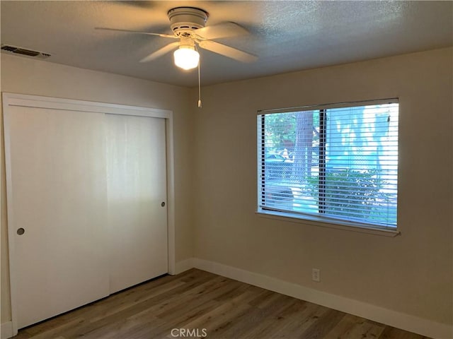 unfurnished bedroom with a textured ceiling, baseboards, light wood-type flooring, visible vents, and a closet