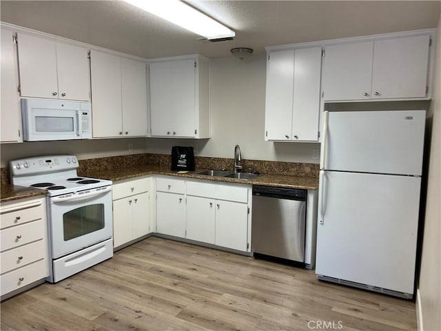 kitchen with dark countertops, a sink, white appliances, white cabinetry, and light wood-type flooring