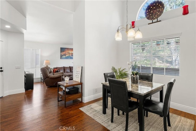 dining area featuring baseboards, dark wood finished floors, an inviting chandelier, and a high ceiling