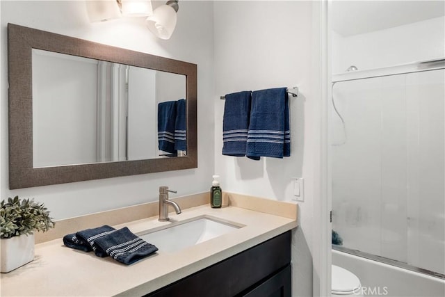 bathroom featuring vanity, enclosed tub / shower combo, and toilet