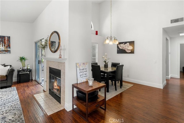 living area featuring an inviting chandelier, a fireplace, wood finished floors, a towering ceiling, and visible vents