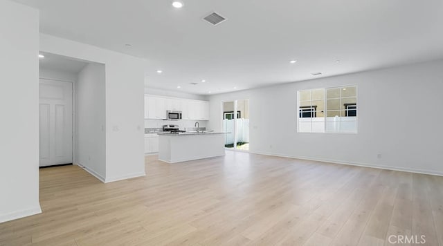 unfurnished living room featuring a sink, light wood-style flooring, recessed lighting, baseboards, and visible vents