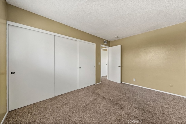 unfurnished bedroom featuring carpet, a closet, a textured ceiling, and visible vents