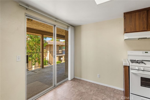 interior space with light countertops, baseboards, under cabinet range hood, and gas range gas stove