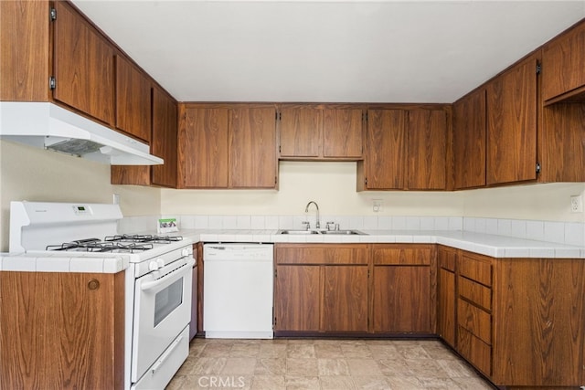 kitchen featuring brown cabinetry, a sink, light countertops, under cabinet range hood, and white appliances