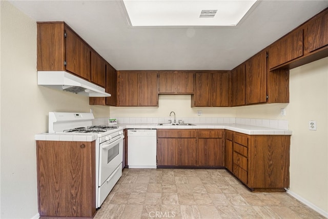 kitchen with stone finish flooring, visible vents, a sink, under cabinet range hood, and white appliances