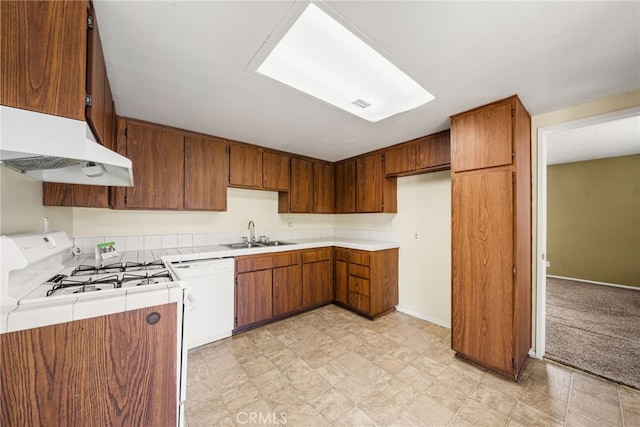 kitchen featuring brown cabinets, a sink, white appliances, tile countertops, and under cabinet range hood