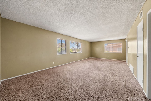 carpeted empty room featuring baseboards, a textured ceiling, visible vents, and a wealth of natural light