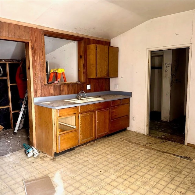 kitchen with a sink, brown cabinetry, wooden walls, and lofted ceiling
