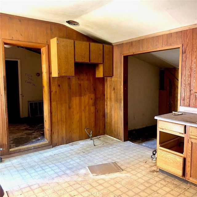 kitchen featuring brown cabinetry, wood walls, light floors, and lofted ceiling